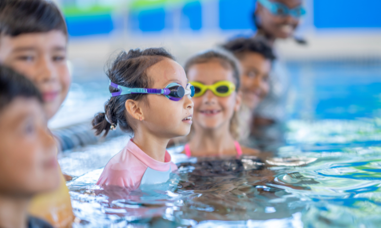 أطفال يسبحون في مسبح مائي، في سياق توضيح هل السباحة او الماء او الكلور يمكن أن تقتل القمل أو تؤثر على بقائه في الشعر.